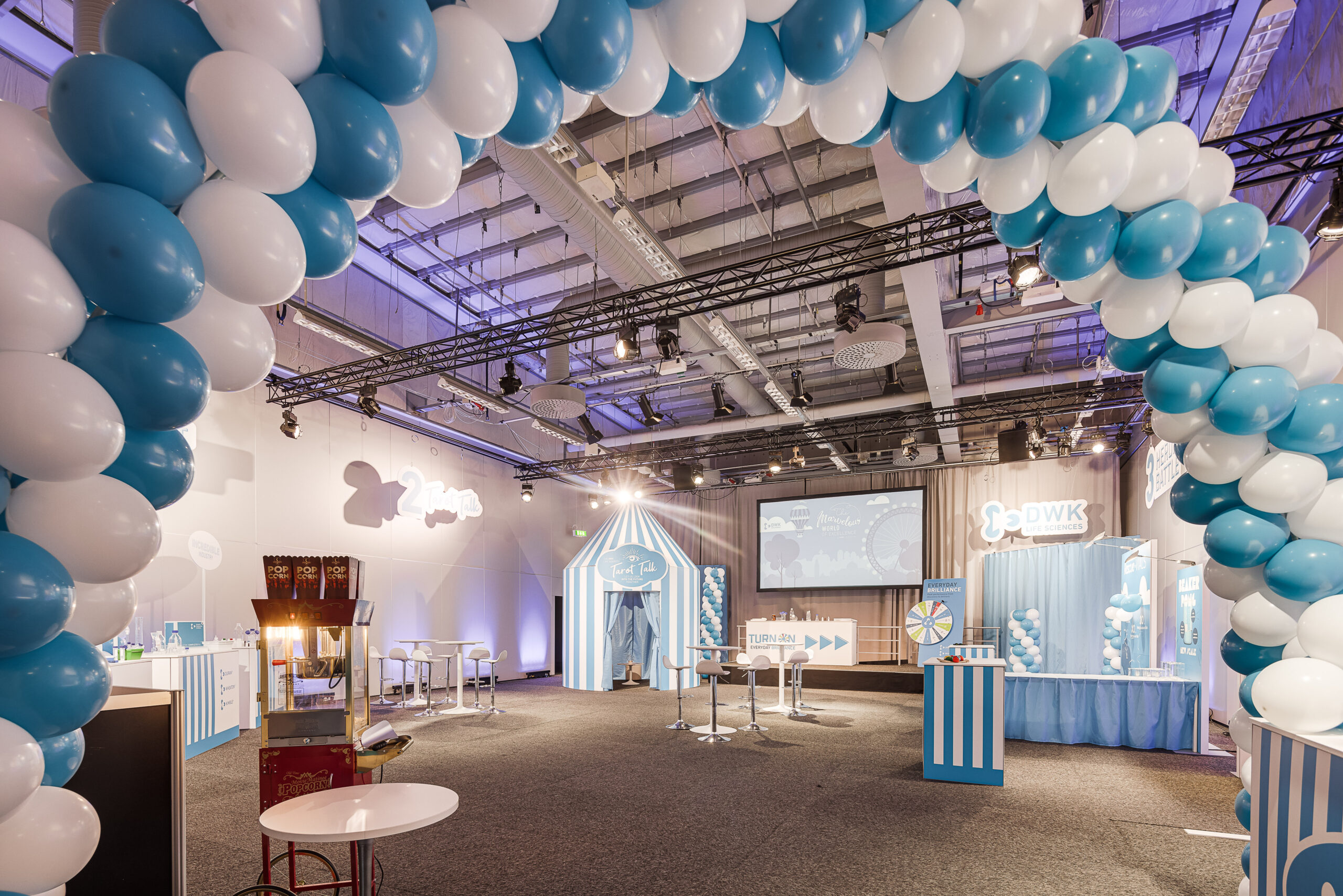 Stor ballongbåge i blått och vitt som leder in till en mässyta med lekfull design