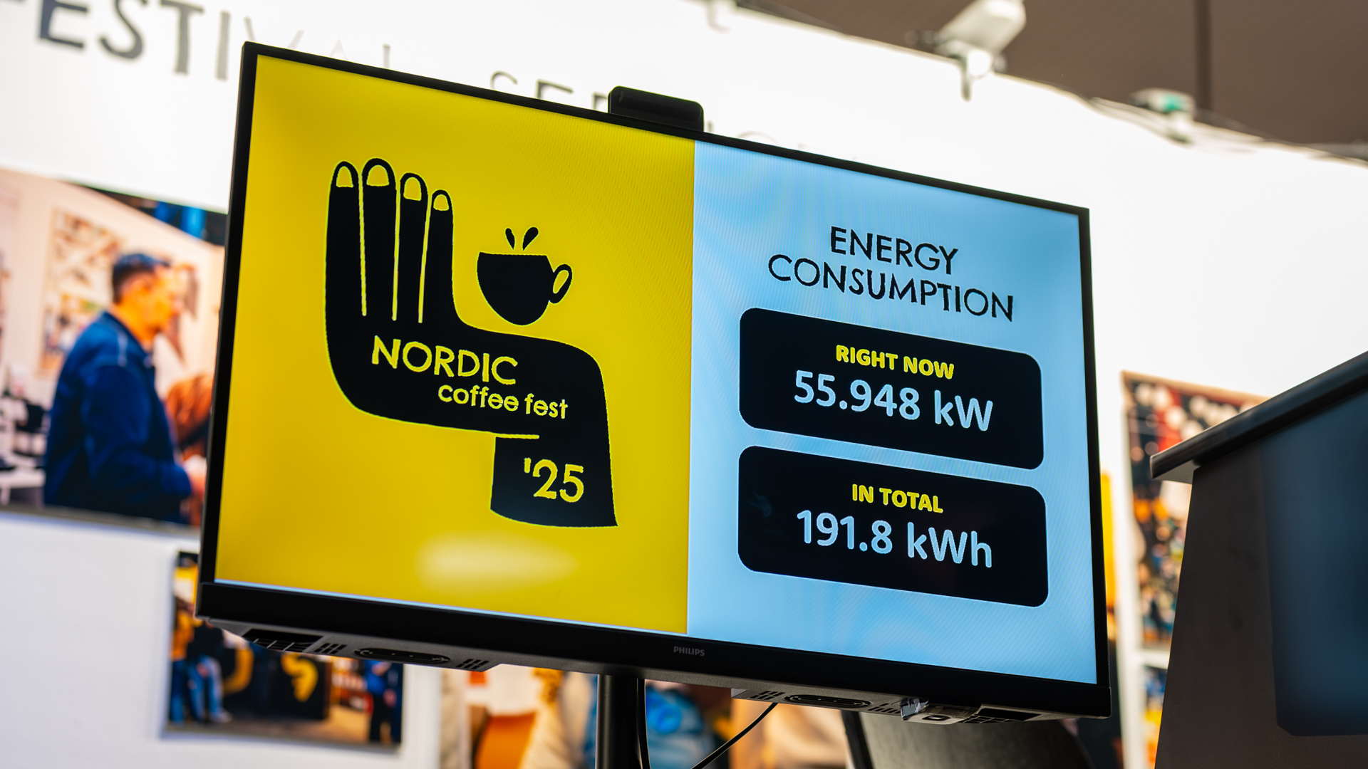 A screen displays “Nordic Coffee Fest 25” with a coffee cup graphic on the left, and energy consumption stats on the right: “Right now: 55.948 kW” and “In total: 191.8 kWh.”.