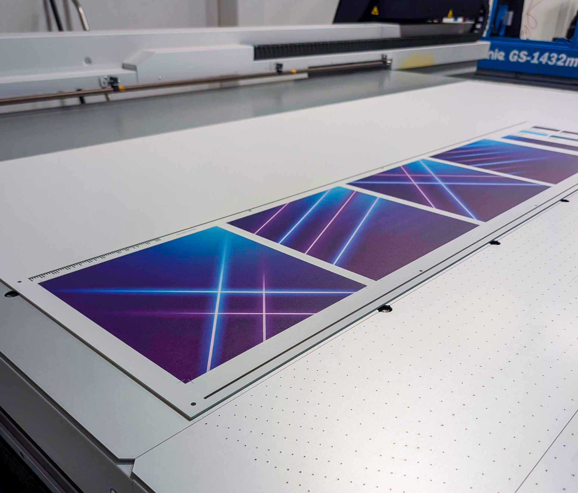 A sheet with three printed images of diagonal neon lines on a purple background lies on the flatbed of a large-format printer in a print shop.