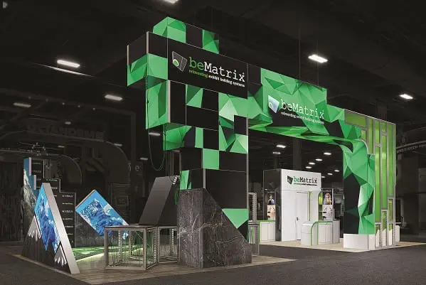 Trade show booth for beMatrix features geometric green panels, digital displays, and a prominent archway with the beMatrix logo and slogan “the original frame system.” The design is modern and eye-catching.