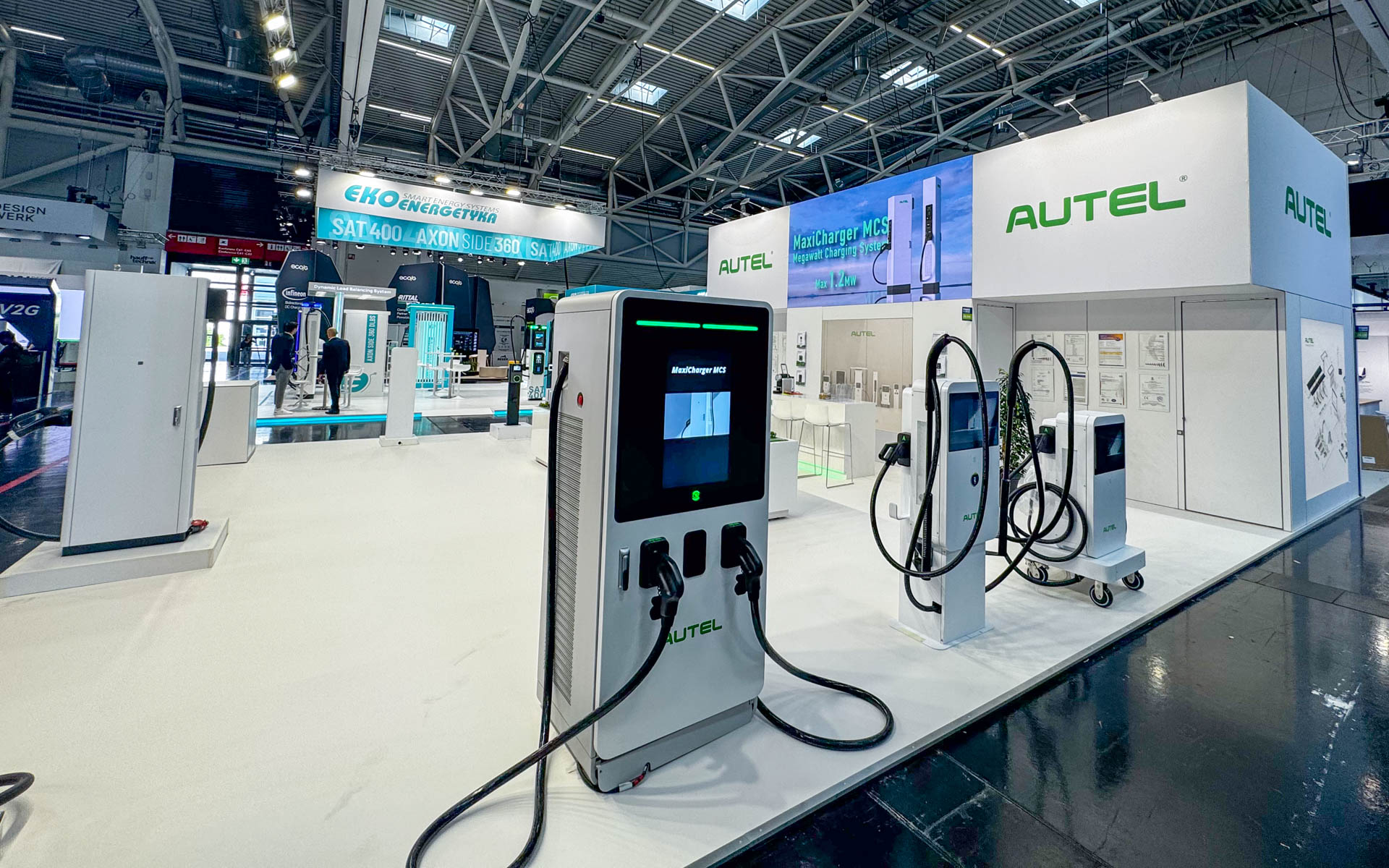 Modern exhibition booth displaying electric vehicle charging stations by AUTEL, with sleek white and green design, digital screens, and charging cables, set in a bright, spacious trade show hall.