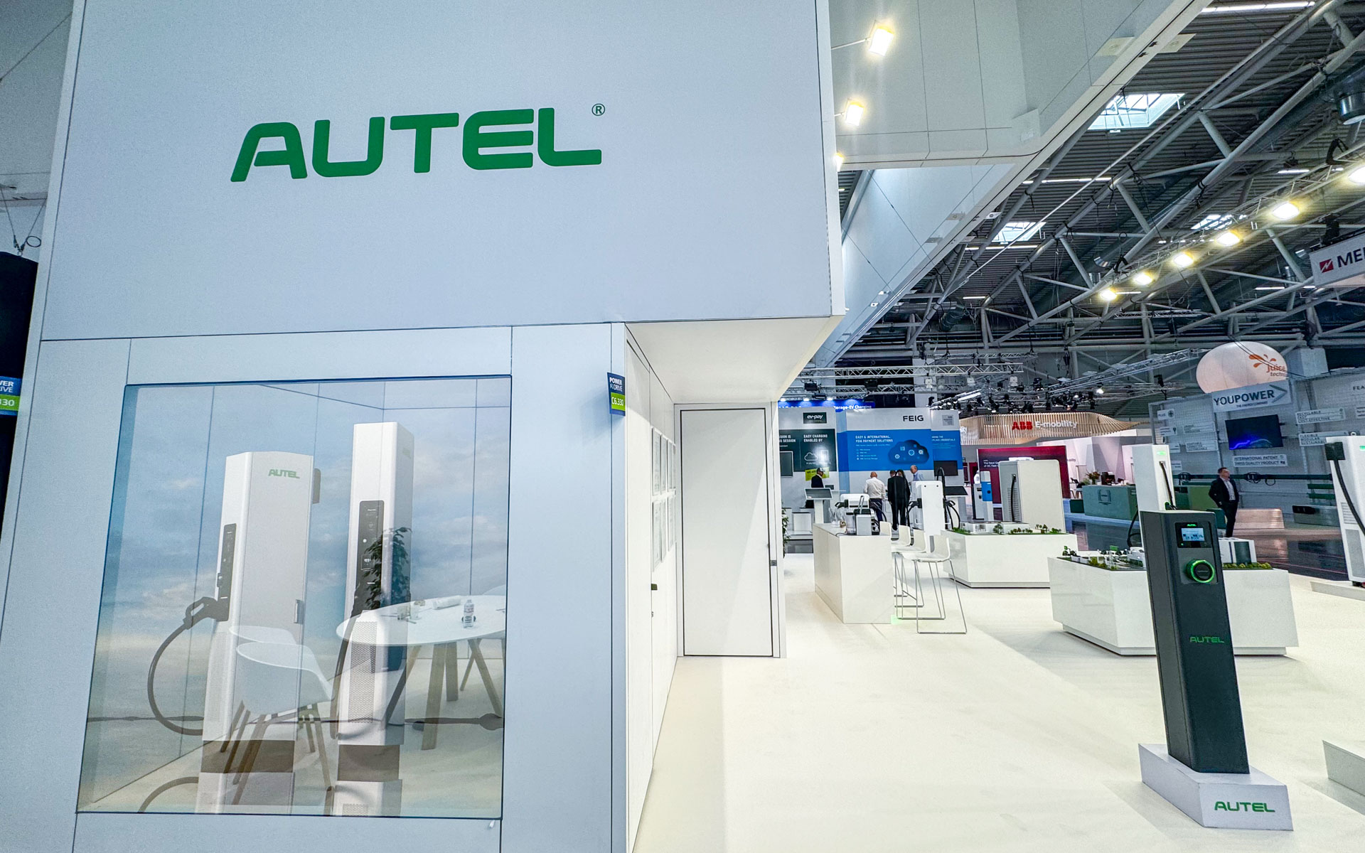 A modern exhibition booth with the green AUTEL logo, displaying electric vehicle chargers. The booth features glass walls, white furniture, and a clean, bright design at a technology trade show.