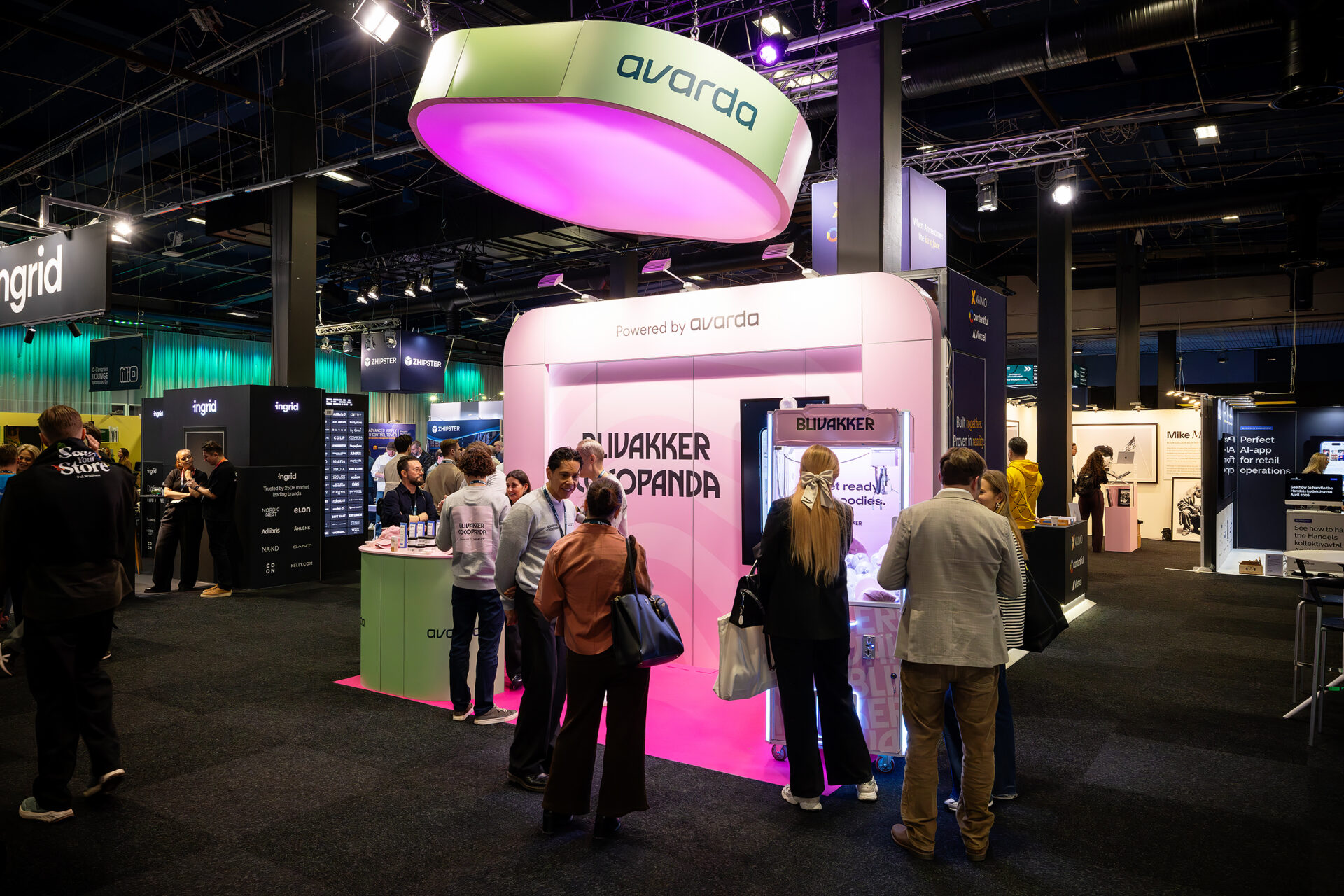 People gather around a brightly lit exhibition booth labeled AVARDA and AWAKER PANDA at a busy indoor trade show, with other illuminated booths and signs visible in the background.
