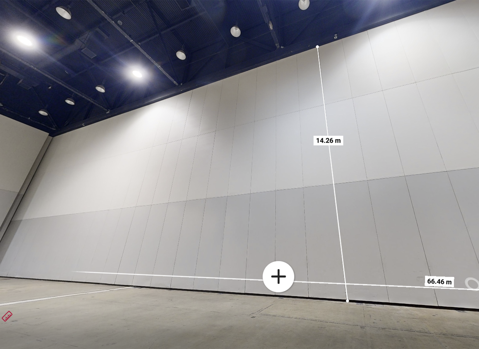 A large, empty indoor space with a tall white wall; the wall is measured with lines indicating a height of 14.26 meters and a width of 66.46 meters. The ceiling has visible beams and lights.