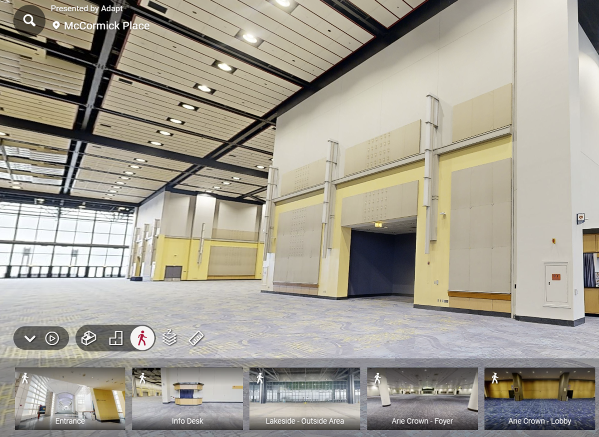 A large, empty convention hall at McCormick Place with high ceilings, yellow and white walls, and gray patterned carpet. Several wide doorways and overhead lights are visible. Small navigation images appear at the bottom.