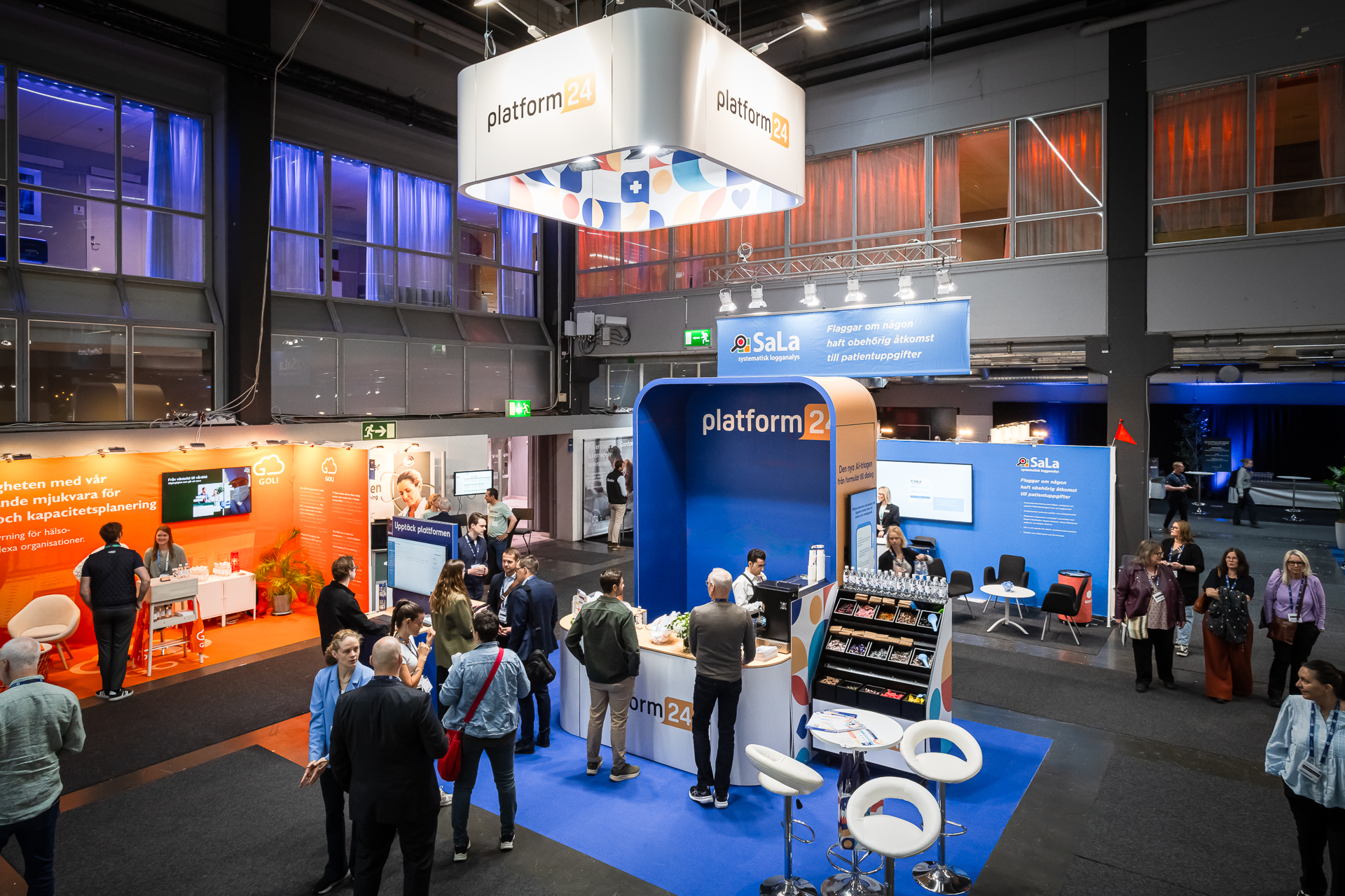 A busy trade show floor with people interacting at a large, modern booth for platform24, featuring branding, digital screens, and displays in a well-lit exhibition hall.