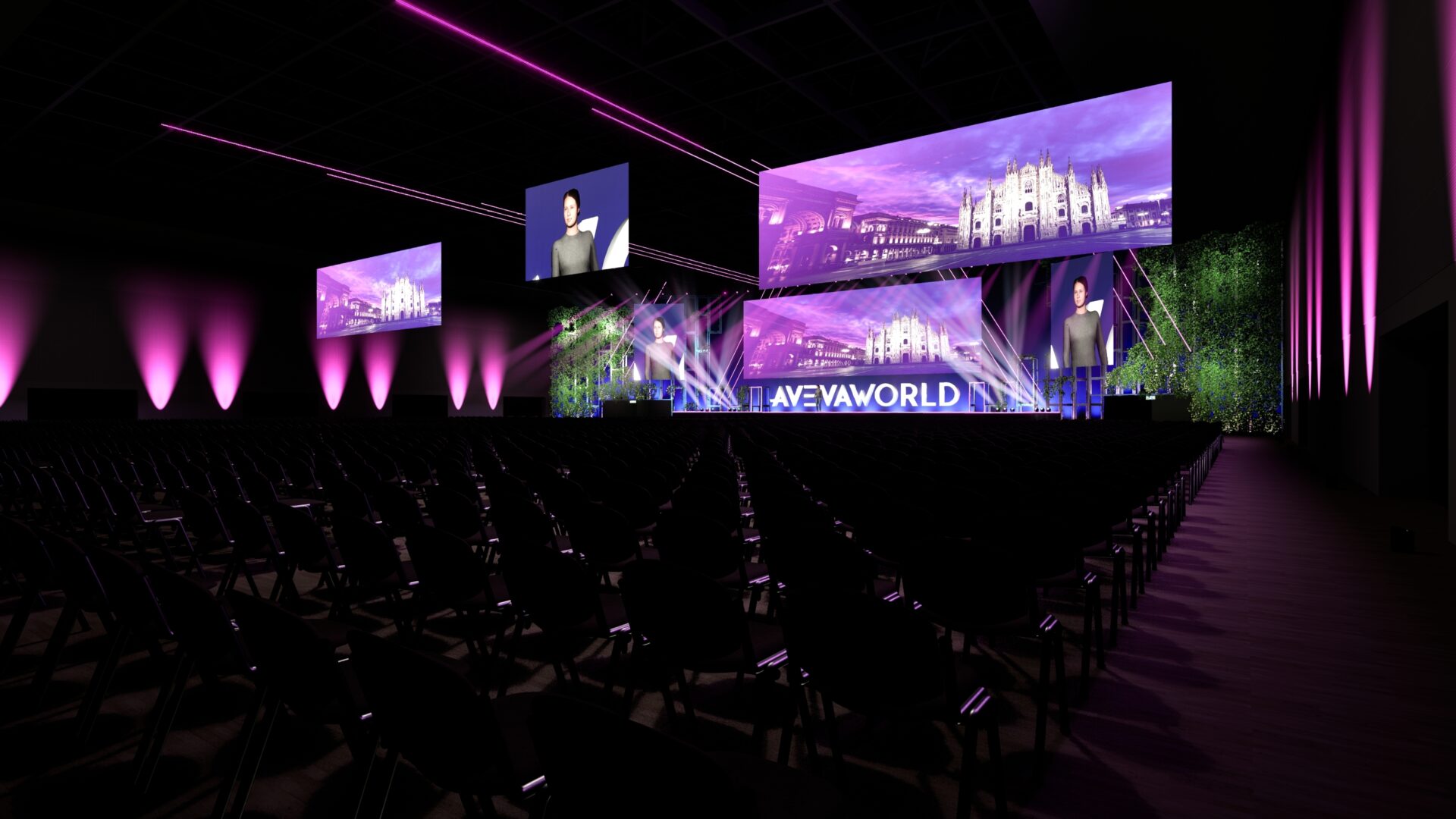 A large, dark auditorium with rows of empty chairs faces a brightly lit stage displaying AVEVA WORLD and large screens showing cityscapes. Pink and purple lights illuminate the stage and walls.
