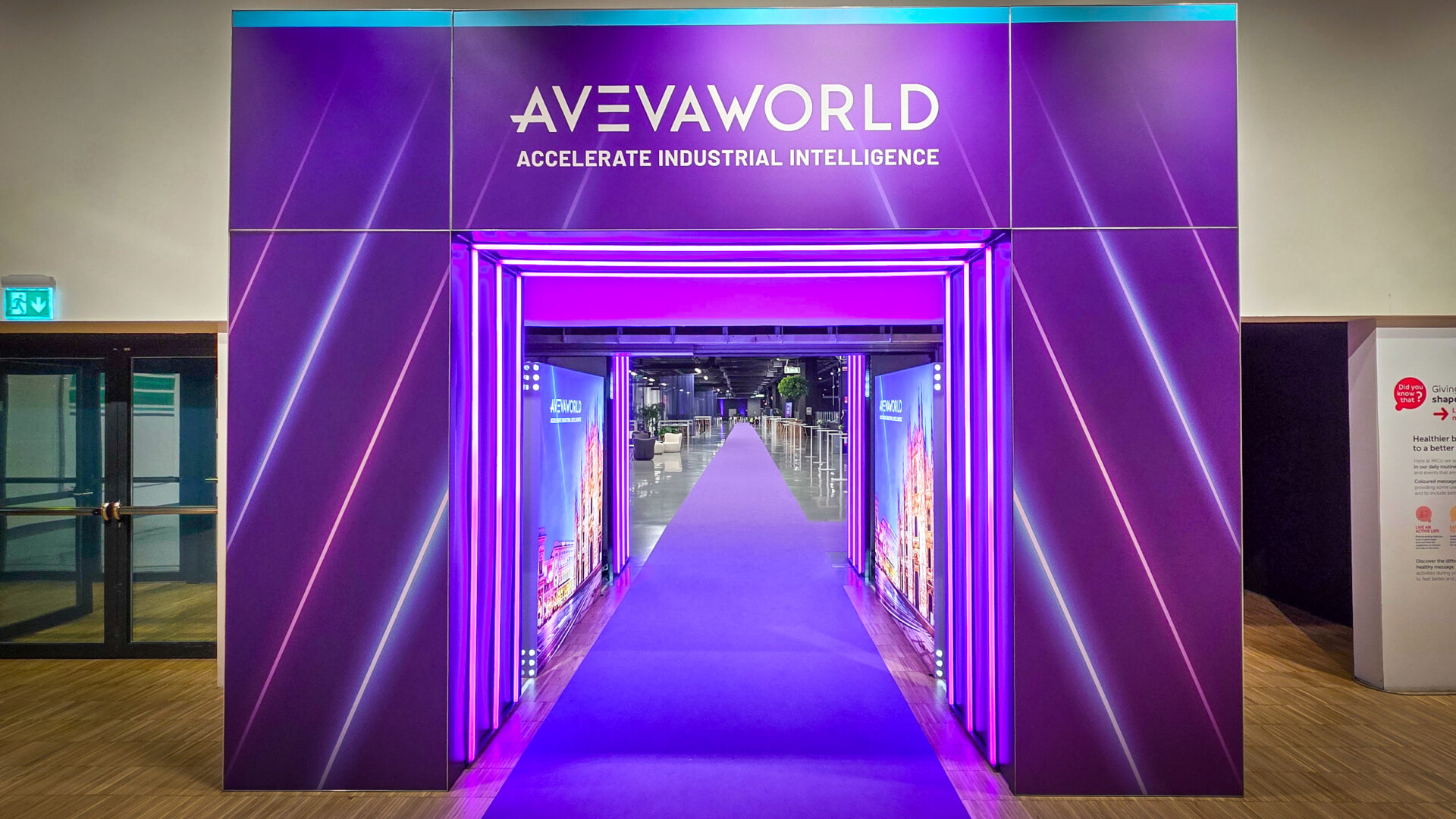 A purple tunnel entrance for AVEVA WORLD with ACCELERATE INDUSTRIAL INTELLIGENCE text. Neon lights line the tunnel.