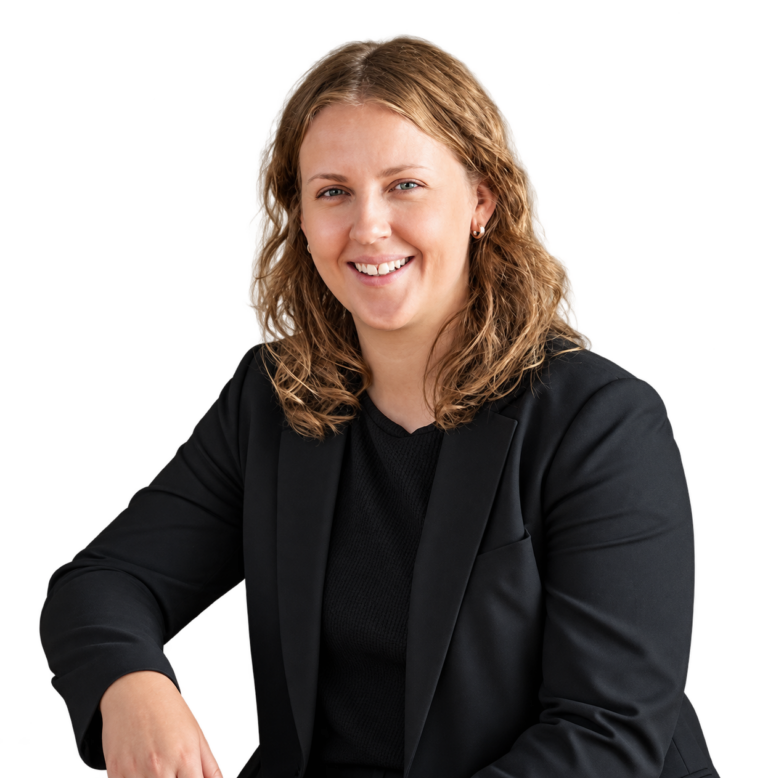 A woman with wavy, shoulder-length light brown hair wears a black blazer and black shirt, smiling at the camera against a plain white background.