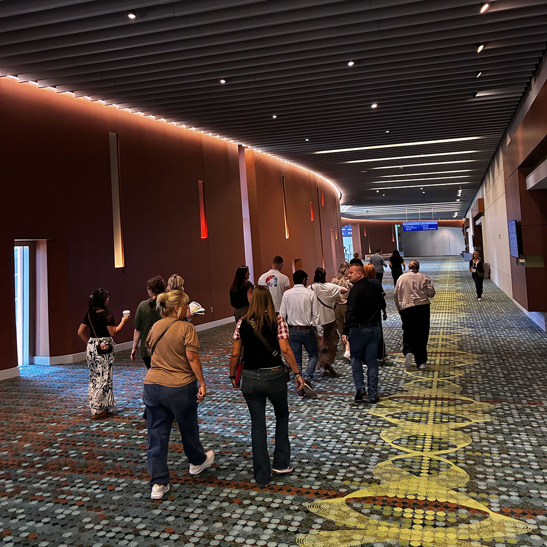 A group of people walks down a long, wide corridor with a patterned carpet and lit-up wall accents.