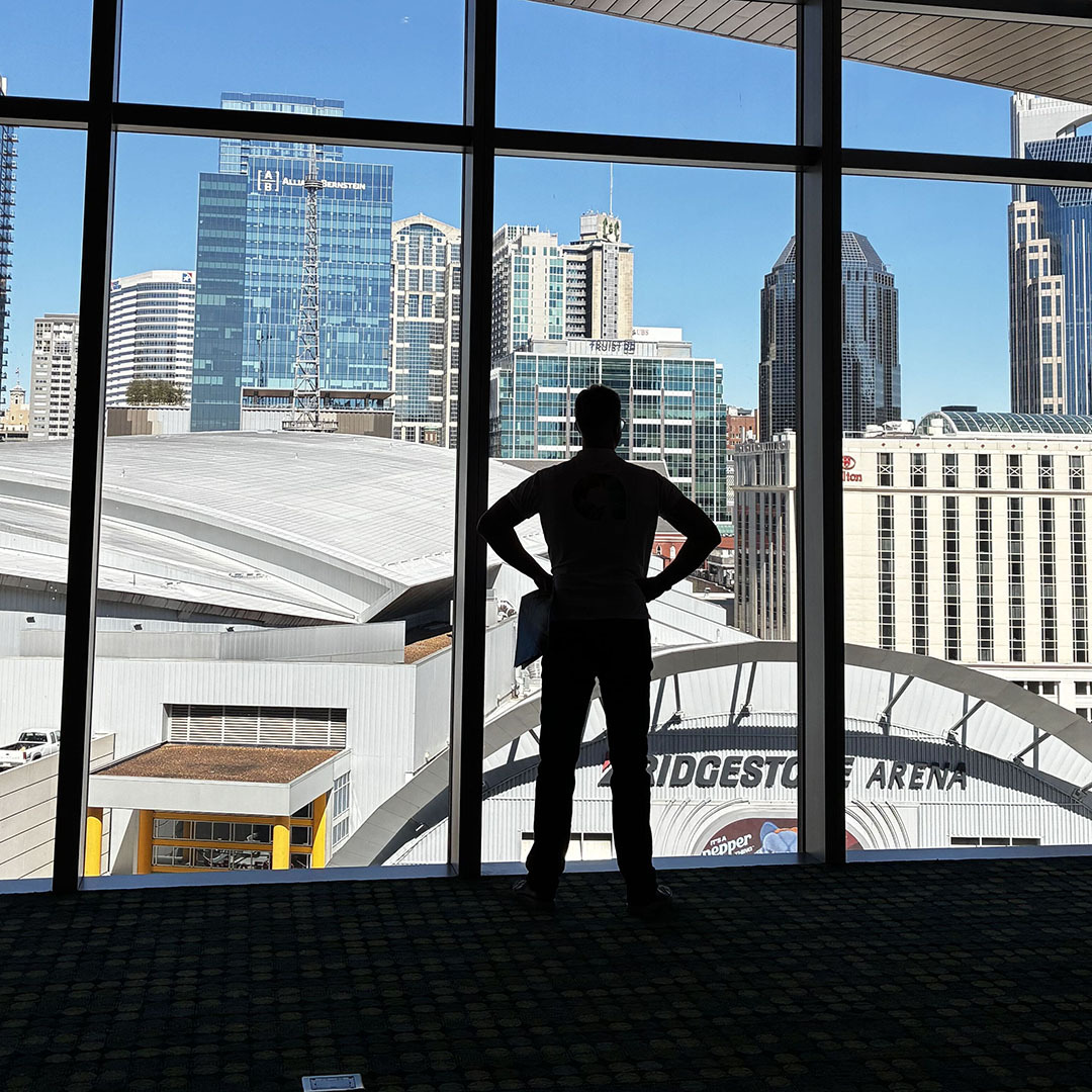 A silhouette of a person standing before a large window overlooking a city skyline and Bridgestone Arena.